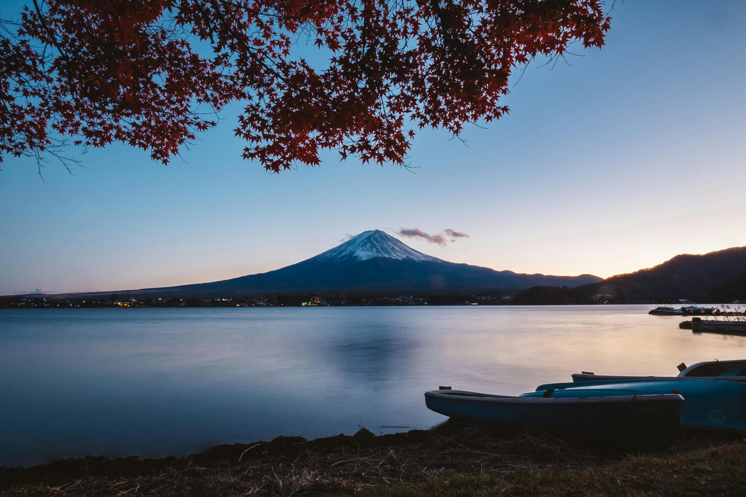 Mount Fuji at dusk viewed from Lake Kawaguchi, with autumn leaves and canoes in the foreground